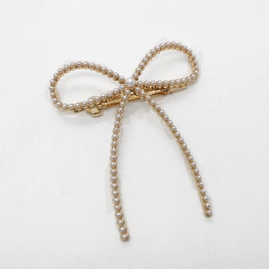 Détail d'une pince à cheveux nœud doré ornée de perles blanches et fermoir ressort