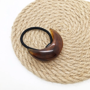Detail of tortoise shell resin crescent moon on a black elastic hair tie with rope base