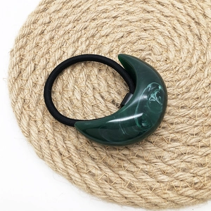 Detail view of dark green resin crescent hair tie with marble texture on straw mat
