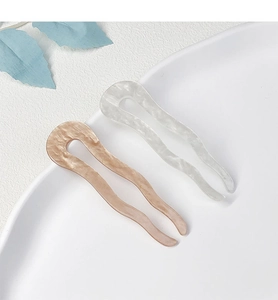 Close-up of pink and white marble texture wavy acetate U-shaped hair pins in a ceramic tray
