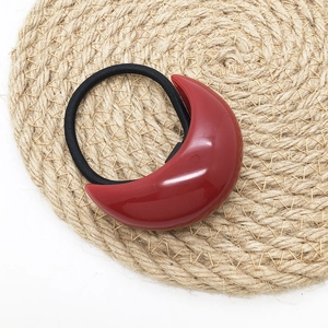 Close-up of a minimalist black elastic hair tie with a glossy red crescent-shaped resin charm
