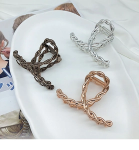 Three elegant twisted metal hair claws in gun black, silver, and rose gold on a ceramic tray