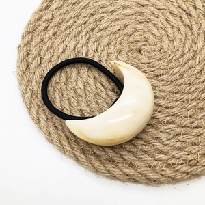 Close-up of cream U-shaped marble resin charm on a black elastic hair tie for women