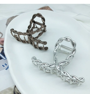 Detailed view of silver and bronze metal hair claws with twisted chain design on a tray