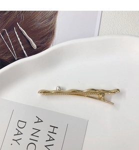 Detailed view of a gold-plated wavy hair clip with a pearl accent on a ceramic tray