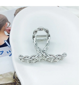 Close-up of a silver braided metal hair claw clip displayed on a white ceramic plate