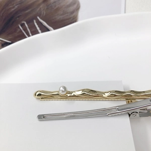 Gold wavy hair clip with pearl and silver duckbill clip on minimalist ceramic tray