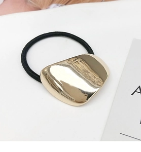 Detail of a minimalist gold geometric metal hair tie with a black elastic band on white