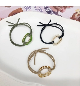 Three elastic hair ties in green, black, and beige with resin oval rings in a ceramic tray