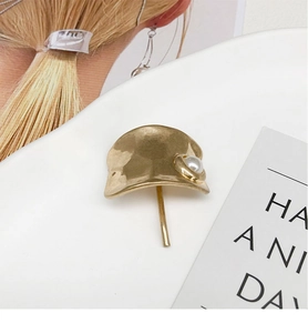 Detailaufnahme einer gehämmerten goldenen Haarmanschette mit weißer Perle und Stecknadel