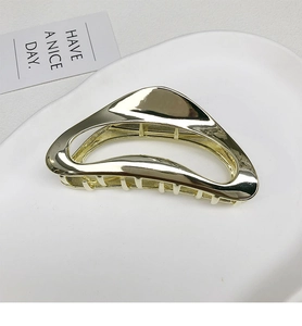 Macro detail of a golden geometric metal hair claw clip with mirror finish on white plate