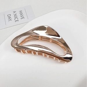 Close-up of rose gold metal shark hair claw clip with irregular hollow design on white ceramic plate