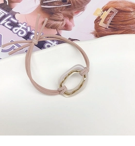 Close-up of pink elastic hair tie with oval acetate charm and golden metal ring