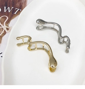 Détail de pinces à cheveux ondulées en or et argent dans une coupelle en porcelaine