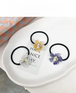 Detalle de tres gomas de pelo de flores con perlas y pétalos de resina en plato cerámico