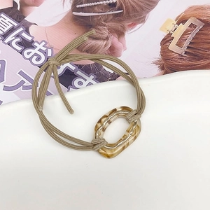 Close-up of khaki elastic hair tie with amber acetate ring and wavy gold metal detail