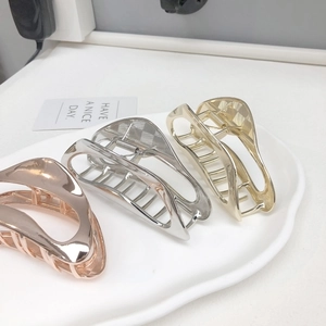 Three elegant minimalist metal hair claws in gold, silver, and rose gold on a ceramic tray
