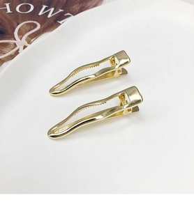 Detailed view of two polished gold wavy hair clips on a minimalist ceramic plate