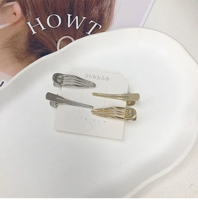 Detailed view of gold and silver wave hairpins on a white display card in a ceramic tray