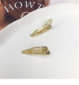 Detailed macro shot of gold-finished wavy and textured metal hair clips on a white plate