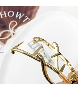 Vue macro d'une pince à cheveux en métal doré poli avec logo entrelacé sur céramique