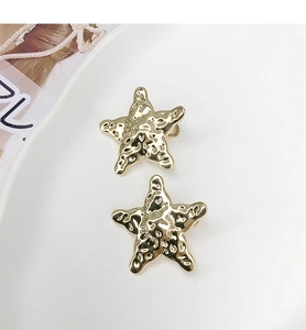 Gros plan de boucles d'oreilles étoile de mer dorées avec texture irrégulière sur plat