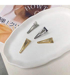 Dettaglio di quattro fermagli per capelli a triangolo in metallo oro e argento testurizzato