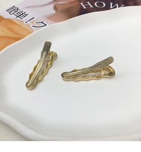 Dettaglio di due fermagli per capelli dorati a onde con trama a griglia su piatto bianco