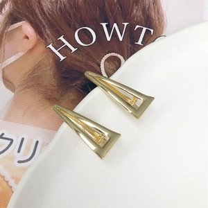 Dettaglio di fermagli per capelli a triangolo dorato in lega su supporto bianco curvo