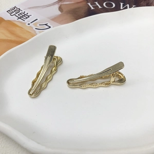 Set di due fermagli per capelli a coccodrillo dorati con bordi ondulati su piatto
