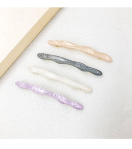 Close-up of four wavy acetate hair clips in peach, grey, cream, and purple marble textures