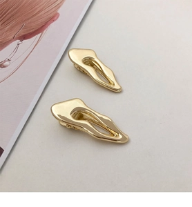 Detail view of two gold irregular wavy hair clips with a polished metallic finish