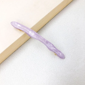 Macro shot of wavy lavender hair clip with marble texture and golden metal spring clasp