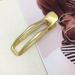 Macro view of a gold-plated geometric claw clip with a hollow wave design for thick hair