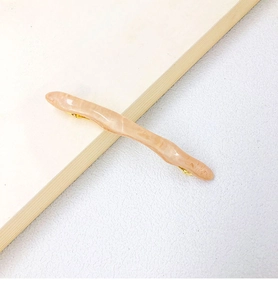 Detail of wavy resin hair clip in marble pink with golden metal spring fastener