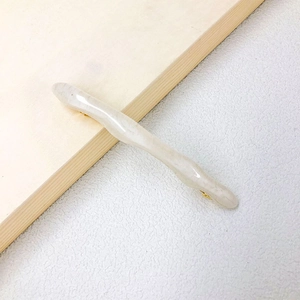 Detail of large wave-shaped cream resin hair clip with gold metal spring clamp