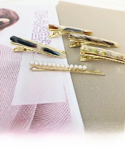 Détail de pinces à cheveux à motif marbre et barrettes en perles sur base dorée