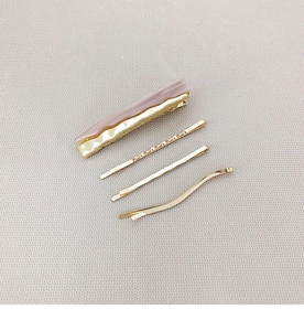 Pink marble resin hair clip set with three golden metallic pins on grey leather background