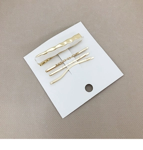 Set of four minimalist gold-tone metal hair clips with white finish on a display card