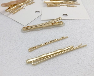 Detail view of golden metal hair pins and marble resin hair clips on textured surface