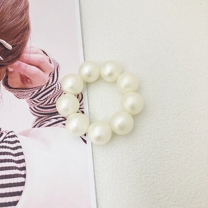 Macro detail of nine cream-colored pearl beads on an elastic hair tie and bracelet