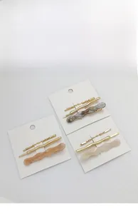 Close-up of stylish resin and metal hair clip sets in amber and cream on white cards