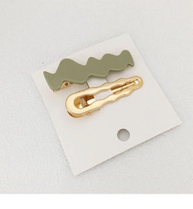 Detail view of wavy hair clips in matte olive green and polished gold finish set