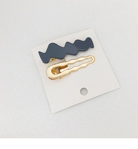 Detail of dark grey matte and golden polished wavy metal hair clips set on card