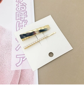 Détail d'un ensemble de barrettes dorées avec texture marbrée et petites perles blanches