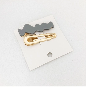 Close-up of a two-piece hair clip set featuring grey resin and gold metal wave designs