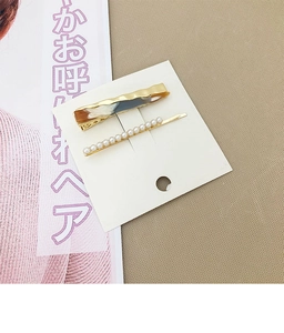 Détail d'une pince à cheveux dorée ondulée et barrette en perles sur carte blanche