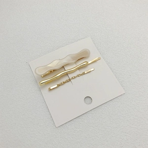 Detailed set of wavy gold metal and cream white acrylic hair clips on a card