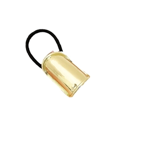 Minimalist gold metal cylinder hair tie with black elastic band on white background