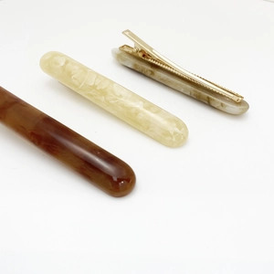 Close-up of three resin hair clips in brown amber, cream, and marble gray with gold metal